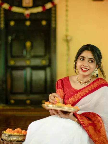 Image of An young and attractive Indian woman in white traditional sari and  red blouse and flowers is smiling while Standing at a Balcony and Posing  for the celebration of Onam/Pongal. Indian